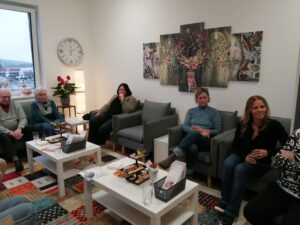 Eine Gruppe von Menschen im Gesprächsrunde bei Prima Magazin in einem gemütlichen Raum mit Snacks und Getränken.