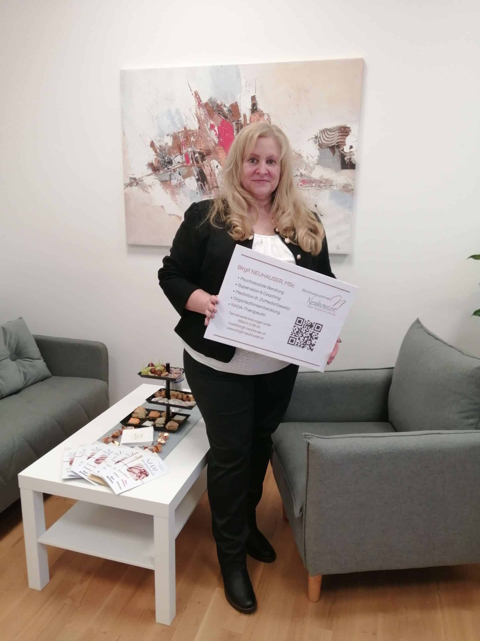 Eine Frau hält ein Schild in einem modernen Raum, umgeben von Prima Magazin-Ausgaben, auf einem Tisch mit Snacks.