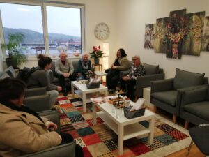 Ältere und jüngere Menschen unterhalten sich in gemütlichem Raum mit Blick auf die Berge, einheimisches Flair bei Prima Magazin.