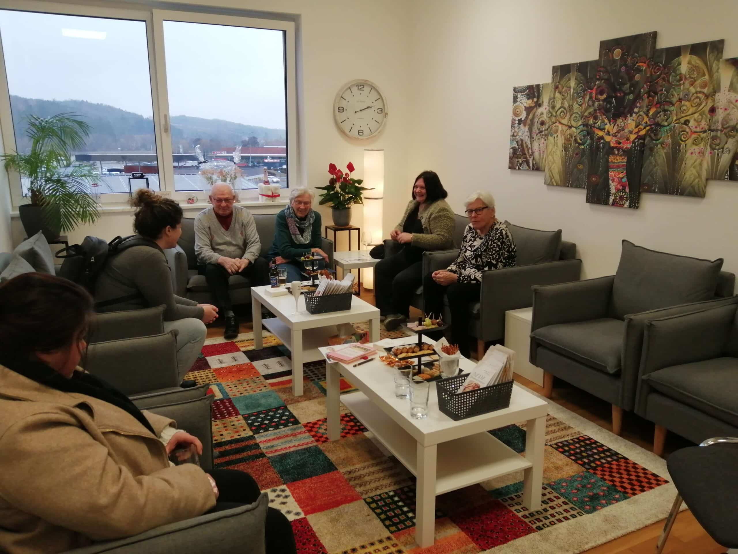 Ältere und jüngere Menschen unterhalten sich in gemütlichem Raum mit Blick auf die Berge, einheimisches Flair bei Prima Magazin.