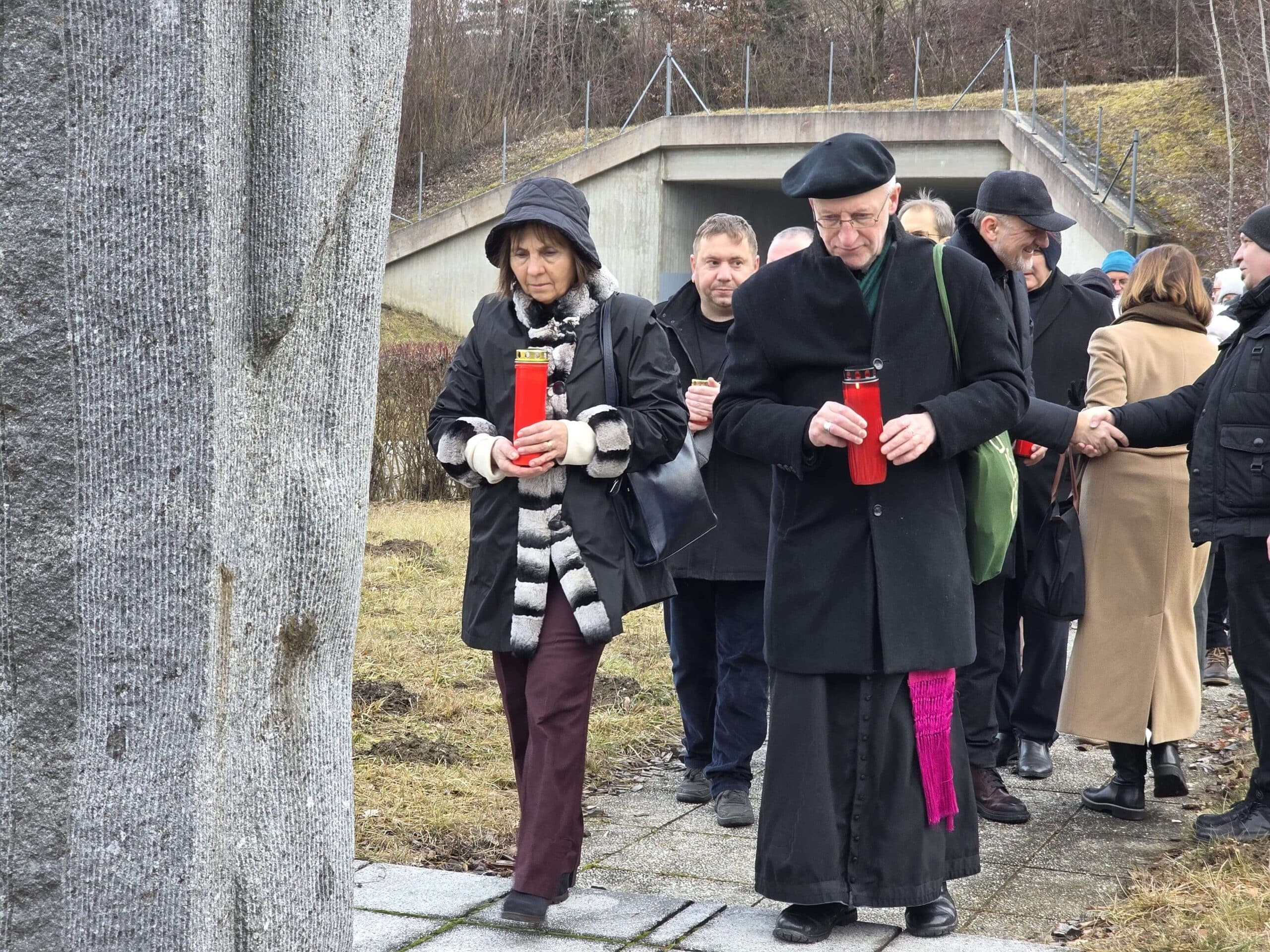 Gruppe von Menschen gedenkt mit roten Kerzen an einem Gedenkort; zeigt gemeinsames Erinnern und regionale Verbundenheit.