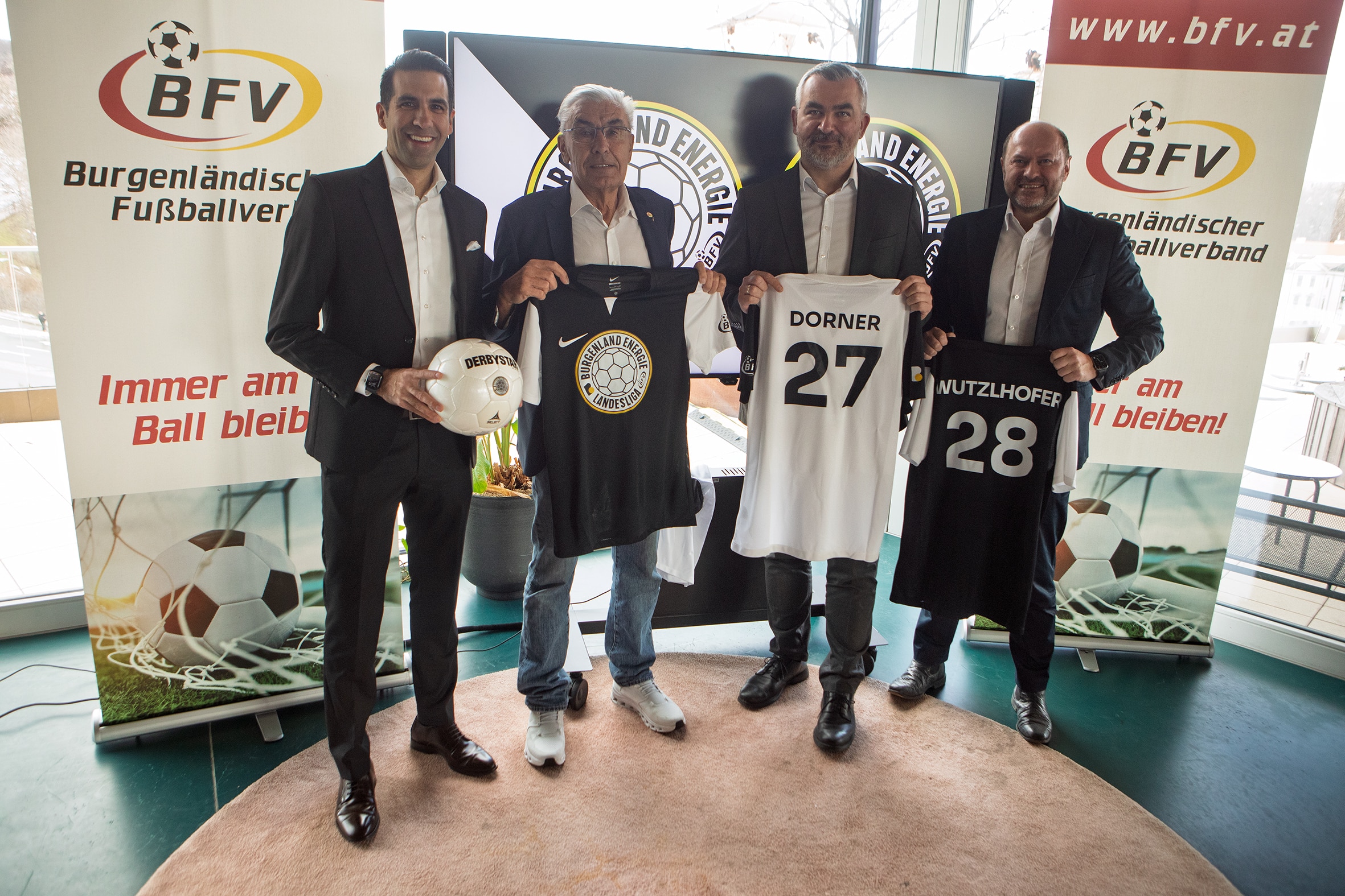 Gruppenfoto von vier Männern bei einer Fußballveranstaltung des Burgenländischen Fußballverbands mit personalisierten Trikots.