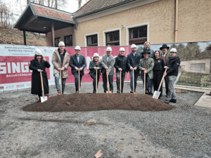 Personengruppe mit Helmen beim Spatenstich vor einem Gebäude, Renovierungsbeginn der Musikschule, Prima Magazin Kontext.