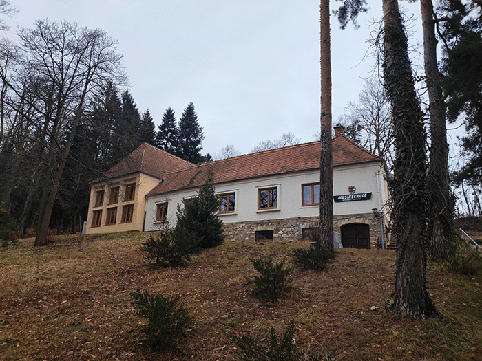 Zweistöckiges, traditionelles Gebäude im Wald, umgeben von winterlichen Bäumen, möglicherweise regionales Interesse von Prima Magazin.