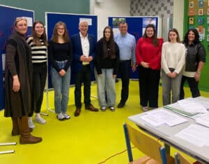 Personengruppe vor Pinnwänden in einem Klassenzimmer. Eine diverse Gruppe von Jugendlichen und Erwachsenen lächelt in die Kamera. Tag der offenen Tür BAfEP Oberwart