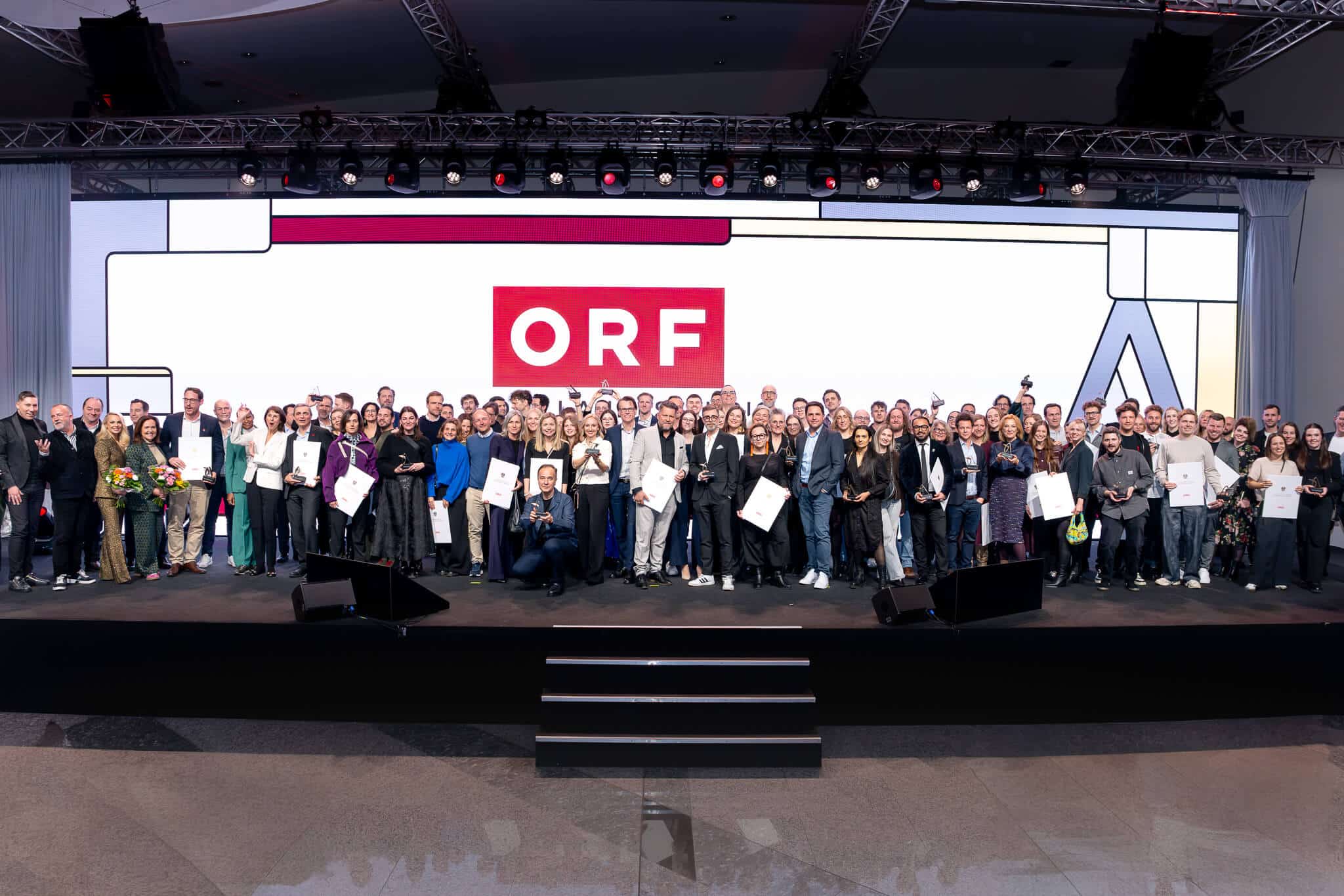 Große Gruppe glücklicher Preisträger auf einer Bühne mit ORF-Logo im Hintergrund, alle halten ihre Auszeichnungen.